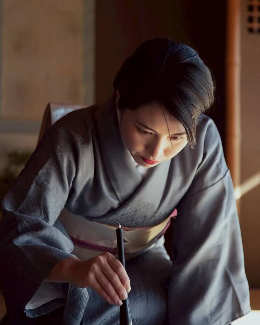 Toshu in kimono bowing over the ink stone in soft light