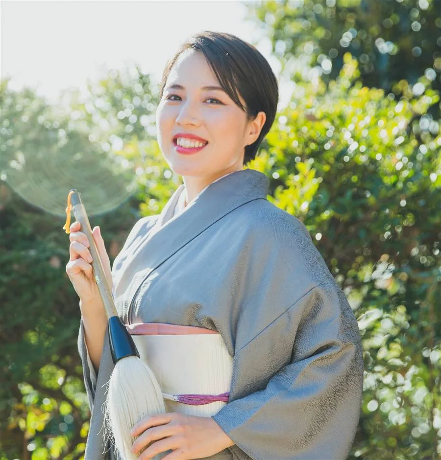 Toshu, smiling in a grey kimono, holding a calligraphy brush